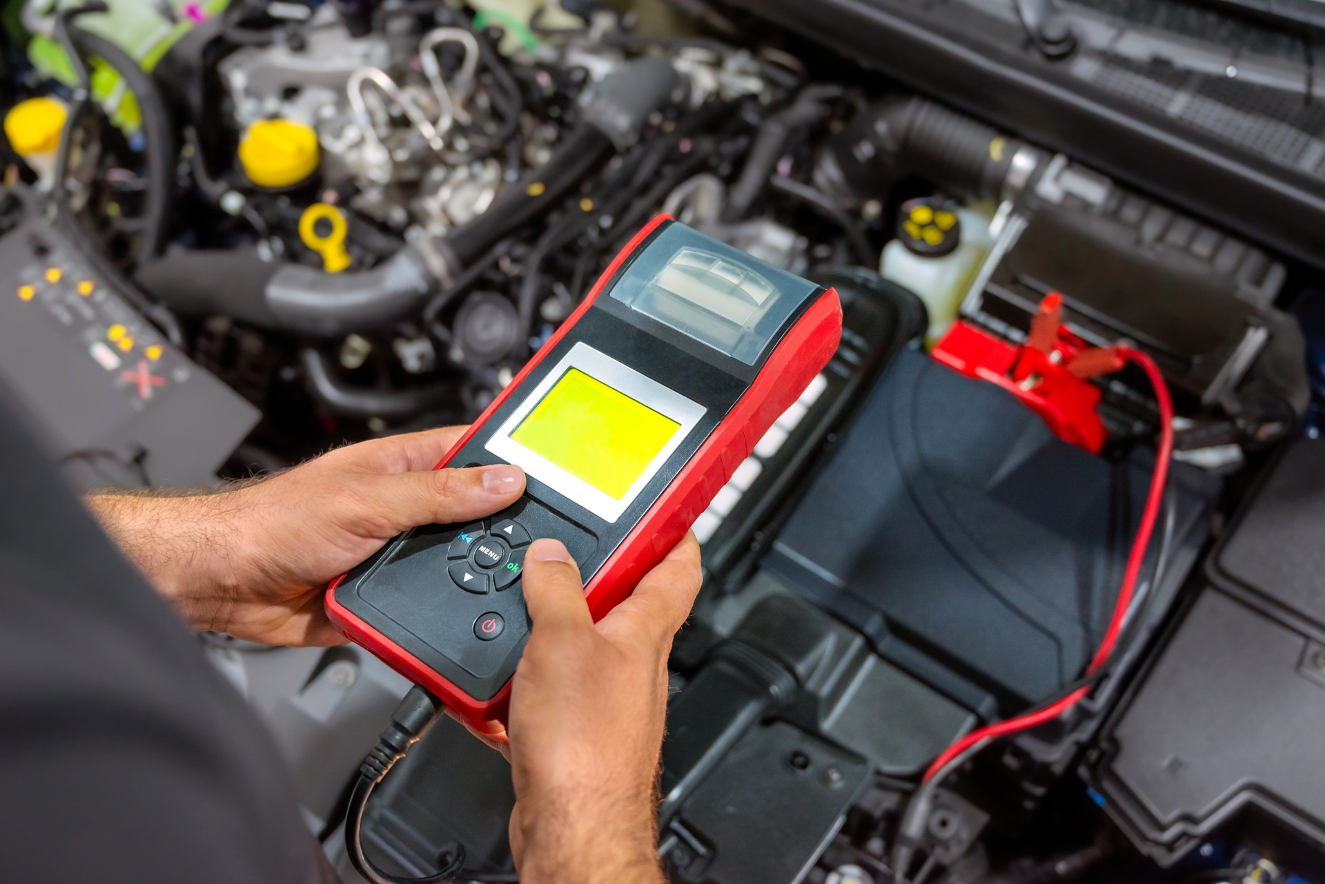 Mechanic measuring car battery voltage with digital multimeter.